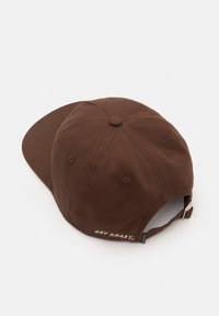 Brun bomullsbasker med krökt skärm, justerbart band i ryggen och broderad text "FÖRBERED DIG" på baksidan. Inkluderar ventilationshål.