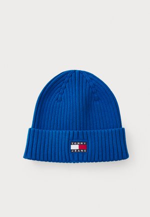 Béret en tricot bleu à côtes, doté d'un revers et d'un patch logo rectangulaire aux rayures rouge, blanche et bleue.