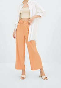 Kevyet, oranssit leveälahkeiset housut, joiden kangas on teksturoitu ja vyötärö korkea, yhdistettynä valkoiseen, löysään paitaan ja kermanvärisiin korkokenkiin.