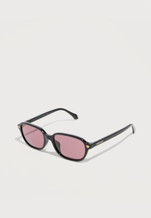 Lunettes de soleil rectangulaires noires avec des verres roses, logos Médusa dorés sur les branches et marquage "Versace" sur la branche droite, présentées sur une surface blanche.