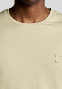 Gaiši zaļa pamata T-krekls ar apaļu kaklu, izgatavots no mīksta kokvilnas. Kreisajā krūtīs neliels izšūts tauriņa logo.