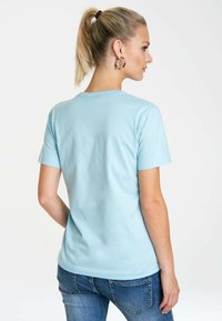 Light blue short-sleeve T-shirt made of cotton. Features a crew neckline and a smooth texture. The model is wearing blue jeans.