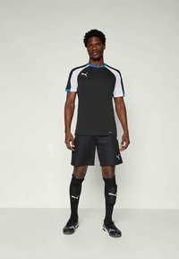 Μαύρη αθλητική μπλούζα με λευκές και μπλε λεπτομέρειες, σε συνδυασμό με μαύρη βερμούδα και κάλτσες. Κατασκευασμένη από ελαφρύ, ύφασμα που απορροφά την υγρασία.