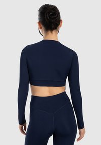 Top corto a maniche lunghe di colore blu navy realizzato in materiale liscio ed elasticizzato, con scollatura rotonda e design aderente, abbinato a leggings a vita alta.