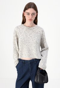 Maglione a maglia chiara con scollo rotondo e maniche lunghe, abbinato a pantaloni a vita alta blu scuro e una piccola borsa nera.