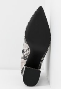 Pointed-toe high heel shoe in black and beige faux snake skin, with a textured rubber sole and a sleek, smooth finish.
