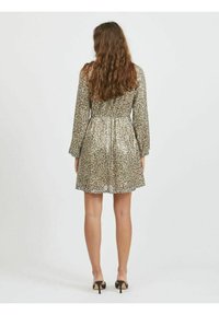 Kortärmad klänning i metalliskt guld med ett leopardmönster. Har en figursydd midja och ett utsvängt kjoldel, som når midjan på låret.