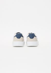 Hvite sneakers med et grått semsket panel og en teksturert marineblå hælkappe. Tykk hvit såle med minimal design og ingen synlig merkevare.