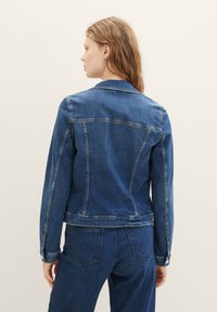 Denim jacket in dark blue with a structured fit, back yoke, and stitched accents. Features long sleeves and button cuffs.