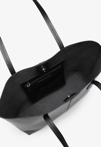 Sac fourre-tout en cuir noir avec deux longues poignées, présentant un intérieur lisse et une poche zippée. Design simple sans accents matériels visibles.