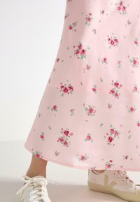 Roze bloemenjurk met een gladde textuur, met kleine rode rozen en groene bladeren. Gecombineerd met witte sneakers met lichtbeige zolen.