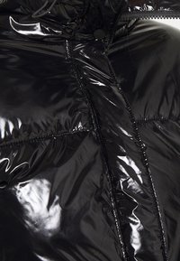 Sort pufferjakke med en skinnende, glat overflade, quiltet tekstur og frontlynlås med trykknaplukning.