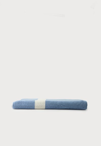 Serviette bleue pliée avec une seule bande blanche placée horizontalement sur un fond blanc uni.