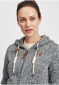Szara dziana bluza z kapturem o fakturowanym wzorze, z przednim zamkiem, beżowymi sznurkami do ściągania z skórzanymi akcentami oraz naszywką z logo na klatce piersiowej.