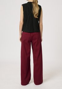 Top negro sin mangas de punto con un patrón de cable texturizado, combinado con pantalones de algodón burdeos de pierna ancha. El conjunto presenta un estilo casual y relajado.