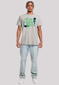 Grå bomull t-skjorte med et fargerikt grafisk trykk som leser "Mester av de mørke kunstene" med tegneserieelementer. Brukt med lyse denimjeans.