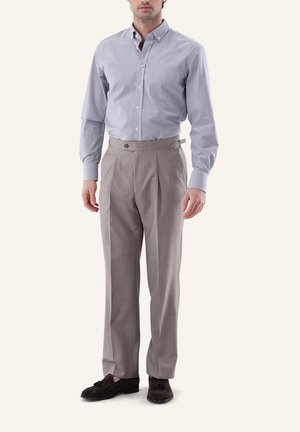 Mann trägt ein hellgraues kariertes Langarmhemd, beige hochtaillierte plissierte Hose mit Seitenverstellern und dunkelbraune Loafers.