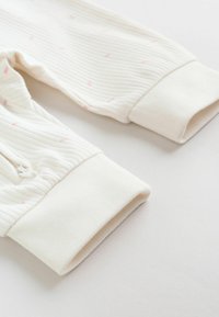 Pantalon bébé en tissu blanc côtelé avec taille et poignets élastiqués, décoré de petits pois roses.