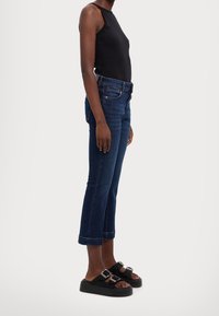 Černý bezramínkový top, tmavě modré džíny a černé texturované šlapky se sponami. Džíny jsou až ke kotníkům s roztřepeným lemem.