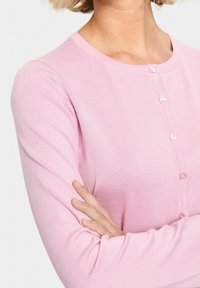 Světle růžový kardigan vyrobený z žebrované látky, s kulatým výstřihem a pěti předními knoflíky, dlouhými rukávy a přiléhavým střihem.