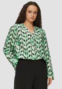 Langärmlige Bluse aus leichtem Stoff, mit einem geometrischen Muster in Grün, Schwarz und Grau. V-Ausschnitt und lockere Passform.