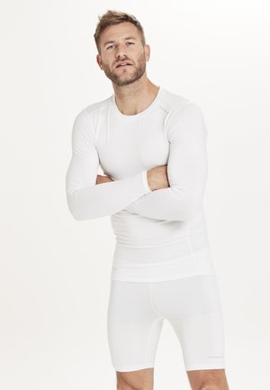 Weißes, langärmliges Sporthemd und kurze Sporthosen aus elastischem Material, mit einer schlanken Passform und glatter Textur. Dezente Markenlogos auf dem Stoff.
