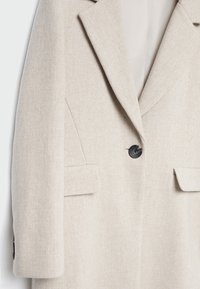 Cappotto in misto lana beige con design su misura, rever a punte, chiusura con un solo bottone nero e due tasche frontali. Texture morbida e linee pulite.