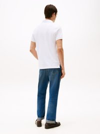 Hvid polo-shirt med korte ærmer, parret med blå denimjeans med lige ben, som har op rullede manchetter, båret med mørke sko.