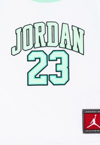 Baltas marškinėliai su mėtinės spalvos užrašu "JORDAN" ir "23" žemiau. Viršutiniame dešiniajame kampe yra raudona ir juoda logotipo etiketė.