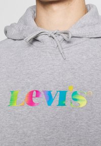 Felpa grigia con tasca a canguro e coulisse. Presenta un logo "Levi's" a gradiente multicolore sul petto. Tessuto morbido.