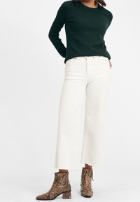 Ciemnozielona, teksturowana bluzka z długim rękawem, oversize'owe białe spodnie z szerokimi nogawkami oraz brązowe botki w wężowy wzór z niskim obcasem.