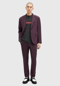 Costume ajusté violet avec une veste et un pantalon assortis, superposé sur un t-shirt graphique noir. Porté avec des chaussures noires et blanches.
