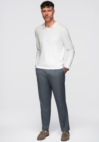 Lichte crème lange mouwen polo met op maat gemaakte grijze broek en bruine suède schoenen, met een casual ontwerp en eenvoudige accenten.