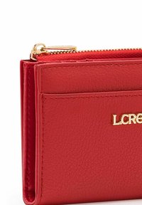 Rote Lederbörse mit einem goldenen Reißverschluss und Logo. Sie verfügt über Kartenfächer und eine strukturierte Oberfläche mit sichtbaren Nähten.
