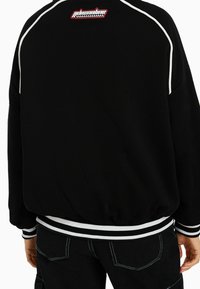 Zwart sweatshirt met witte bies, voorzien van een logopatch op de achterkant. Geribde manchetten en zoom, losse pasvorm en een katoenen mixmateriaal.