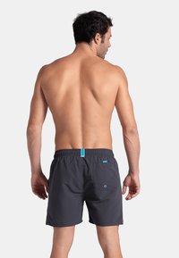 Bañadores de hombre en gris oscuro con una cintura elástica y un acento turquesa. Cuenta con un bolsillo trasero con un ojete decorativo.