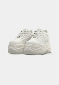 Adidași albi, masivi, cu talpă ridicată, parte superioară dintr-un material sintetic neted, șireturi texturate și detalii subtile ale logo-ului pe limbă.