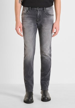 Jeans de denim gris con corte ajustado, acabado desgastado, bolsillos delanteros y costuras en contraste, combinados con botines negros.