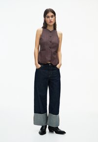 Brun rutig ärmlös topp med framsida knappar, kombinerad med mörkblå vida jeans med grå cuffs och nitar svarta stövlar.