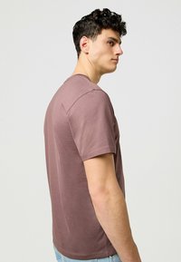 Kortärmad t-shirt i dämpad mauve, rund halsringning, mjukt bomullsmaterial, sid sömsdetaljer, kombinerad med ljus denimjeans.