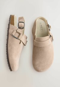 Sabots en cuir suédé beige avec un bout arrondi, une bride à boucle ajustable et une semelle texturée. Doublure intérieure lisse et design minimaliste.
