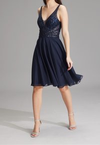 Tummansininen mekko, jonka helmassa on helmikirjailu ja v-pääntie, sekä laskostettu sifonkihame. Yhdistetty hopeisiin nilkkaketjukenkiin.