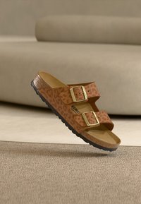 Καφέ σανδάλι τύπου leopard print με δύο ρυθμιζόμενες χρυσές αγκράφες, υφασμένο πάτο και μαύρη λαστιχένια σόλα.