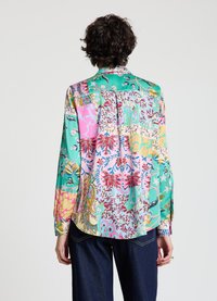 Blouse en soie colorée avec un design patchwork comprenant des motifs floraux rose, vert et bleu. Manches longues, coupe décontractée et ourlet arrondi.