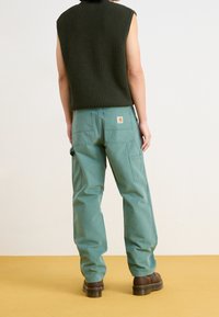 Ärmlös mörkgrön stickad topp och ljusgröna cargobyxor med två bakfickor och sidofickor, kombinerade med mörkbruna skor.