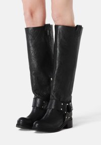 Black leather knee-high boots with a textured finish, wide upper, and adjustable buckle strap featuring metal studs at the ankle.