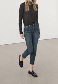 Black long-sleeve shirt paired with dark blue high-waisted jeans and black loafers. The outfit features a checked scarf at the neckline.