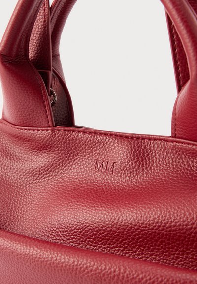 Κόκκινη τσάντα από δερμα με υφή, με κοντά χερούλια, που έχει ανάγλυφα αρχικά γράμματα "MM" στο πάνω μπροστινό μέρος.