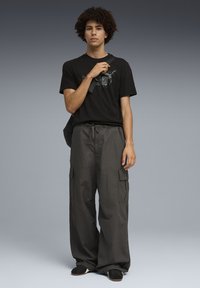 T-shirt en coton noir avec un motif graphique, associé à un pantalon cargo ample gris foncé avec poches latérales et taille à cordon.