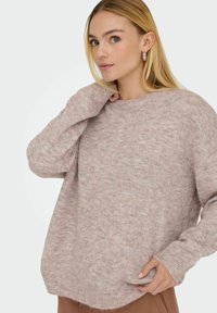 Lyserød strikket sweater med afslappet pasform, lange ærmer, rund halsudskæring og en subtil prikket struktur. Ribkanter ved ærmer og bund.